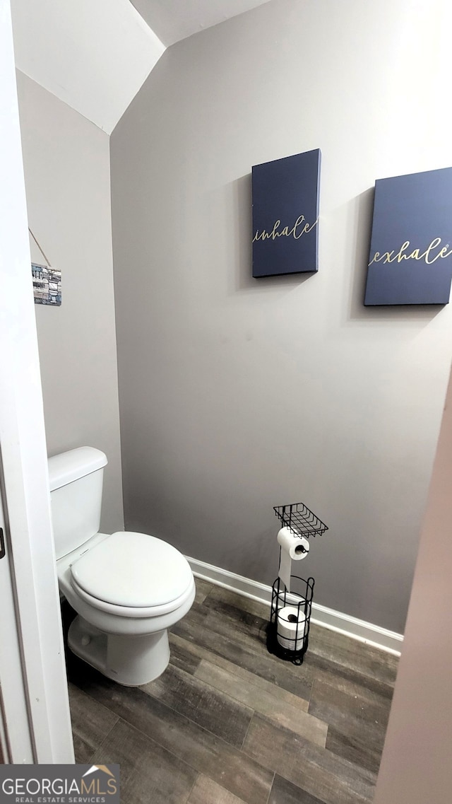 bathroom with vaulted ceiling, wood finished floors, toilet, and baseboards