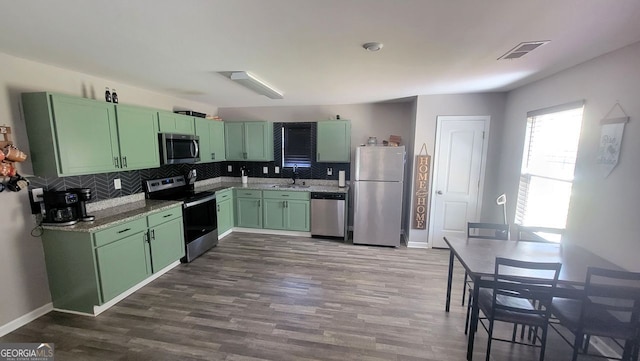 kitchen with a sink, visible vents, green cabinets, appliances with stainless steel finishes, and backsplash