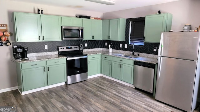 kitchen with wood finished floors, a sink, appliances with stainless steel finishes, tasteful backsplash, and green cabinetry