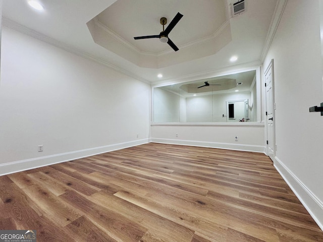 spare room with ceiling fan, wood finished floors, visible vents, ornamental molding, and a tray ceiling