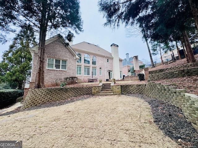 back of house with stairs, a chimney, and brick siding