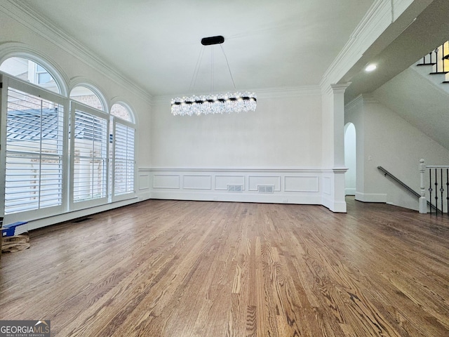 unfurnished dining area with a chandelier, a decorative wall, wood finished floors, and crown molding