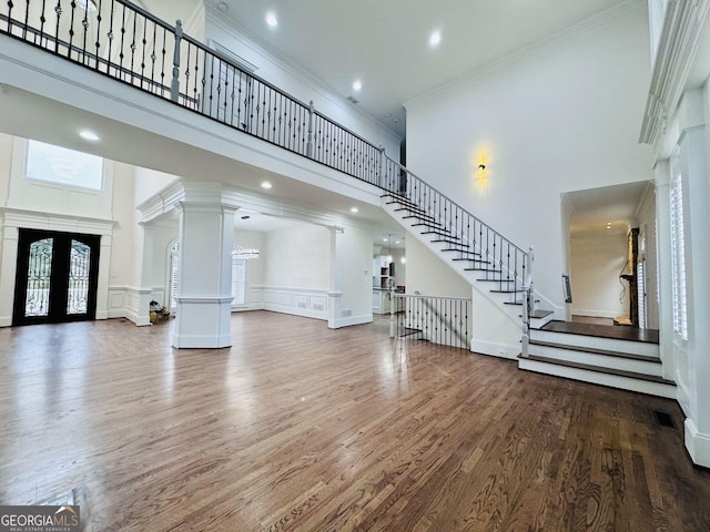 unfurnished living room featuring french doors, a towering ceiling, wood finished floors, ornate columns, and stairs