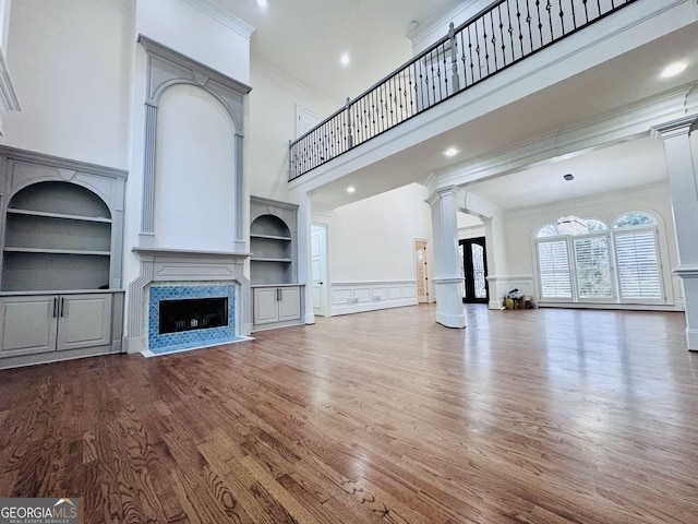 unfurnished living room with built in features, a high ceiling, a high end fireplace, wood finished floors, and ornate columns