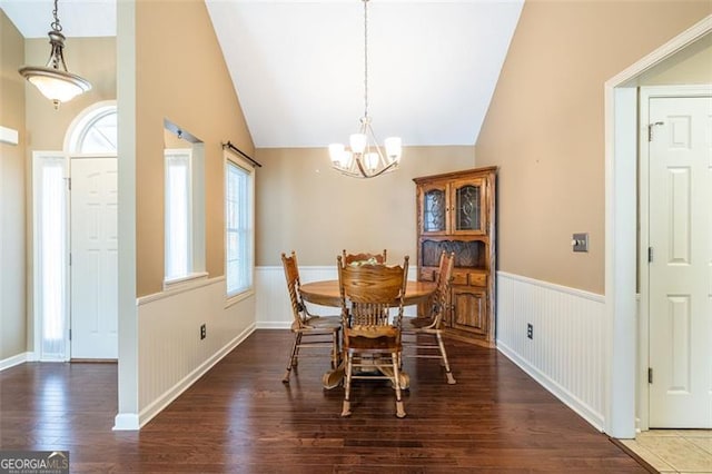 dining room featuring a notable chandelier, vaulted ceiling, dark wood-type flooring, and wainscoting