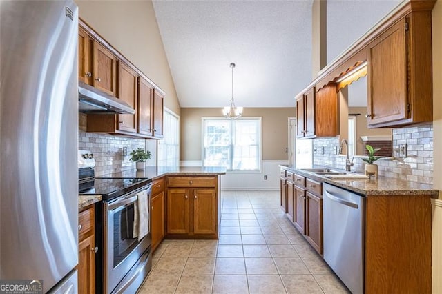 kitchen with under cabinet range hood, stainless steel appliances, a peninsula, a sink, and decorative light fixtures