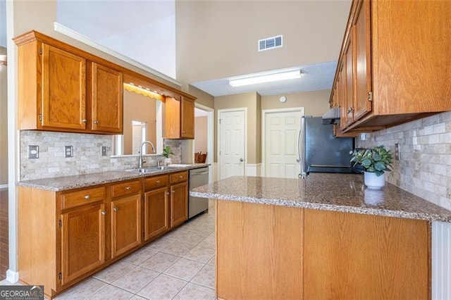 kitchen with visible vents, brown cabinetry, stainless steel appliances, stone counters, and a sink