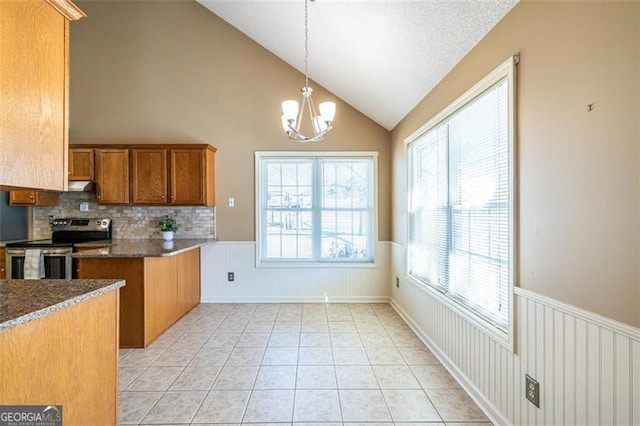 kitchen with light tile patterned floors, dark countertops, a wainscoted wall, decorative light fixtures, and stainless steel electric stove