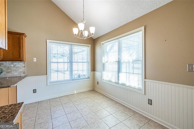 unfurnished dining area featuring light tile patterned floors, a wainscoted wall, an inviting chandelier, vaulted ceiling, and a textured ceiling