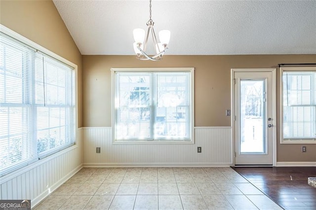 doorway to outside featuring a wealth of natural light, lofted ceiling, and a wainscoted wall