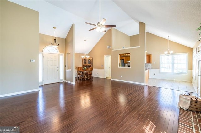 unfurnished living room with baseboards, high vaulted ceiling, wood finished floors, and ceiling fan with notable chandelier