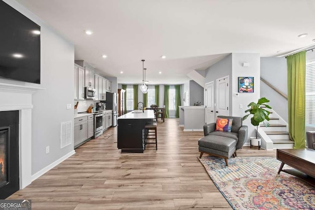 kitchen featuring pendant lighting, a breakfast bar area, light countertops, appliances with stainless steel finishes, and a kitchen island with sink