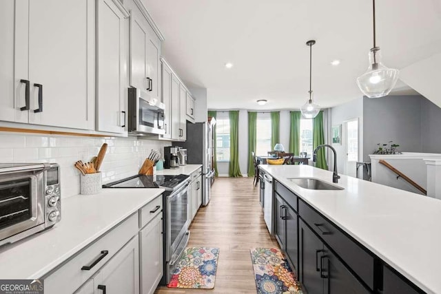 kitchen with stainless steel appliances, light countertops, a sink, and hanging light fixtures