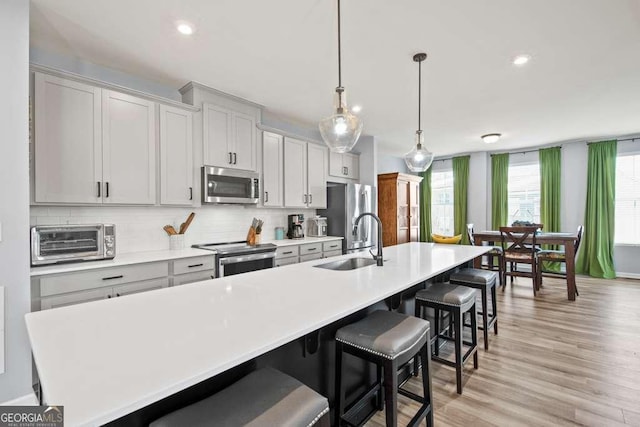 kitchen featuring a sink, a kitchen breakfast bar, light countertops, appliances with stainless steel finishes, and a large island with sink