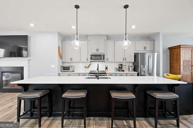 kitchen featuring appliances with stainless steel finishes, white cabinets, light countertops, and a large island with sink