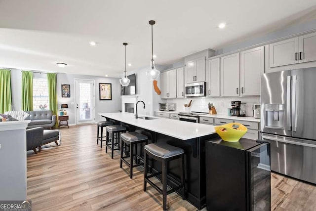 kitchen with appliances with stainless steel finishes, a breakfast bar area, a kitchen island with sink, light countertops, and a sink