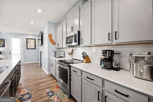 kitchen featuring stainless steel appliances, tasteful backsplash, light countertops, and light wood-style flooring