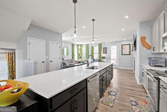 kitchen with stainless steel appliances, light countertops, a sink, and an island with sink