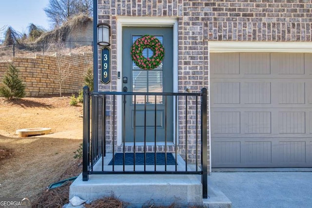 property entrance featuring a garage, brick siding, and fence