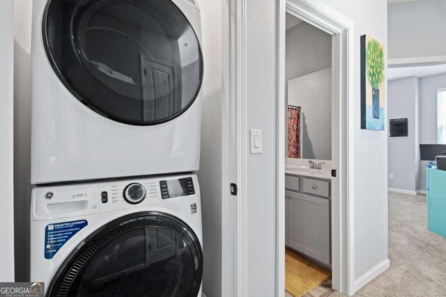 laundry room with light carpet, a sink, stacked washing maching and dryer, laundry area, and baseboards