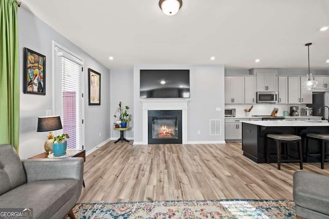 living room featuring recessed lighting, visible vents, light wood-style flooring, a glass covered fireplace, and baseboards