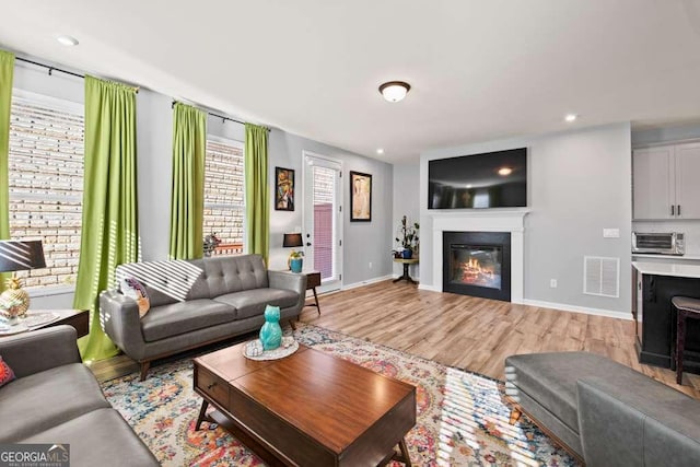 living room featuring a toaster, visible vents, a glass covered fireplace, light wood-type flooring, and baseboards