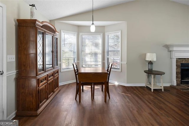 dining space featuring dark wood finished floors, a fireplace, vaulted ceiling, and baseboards