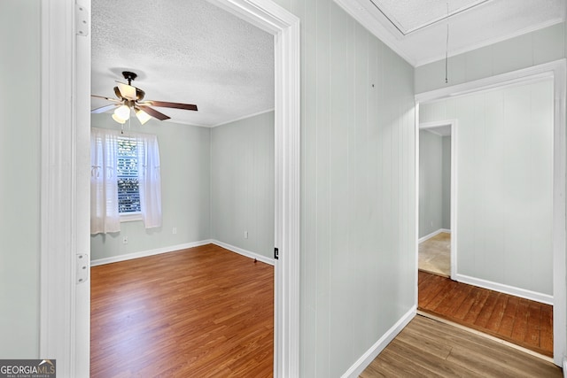 spare room featuring a textured ceiling, wood finished floors, attic access, and crown molding