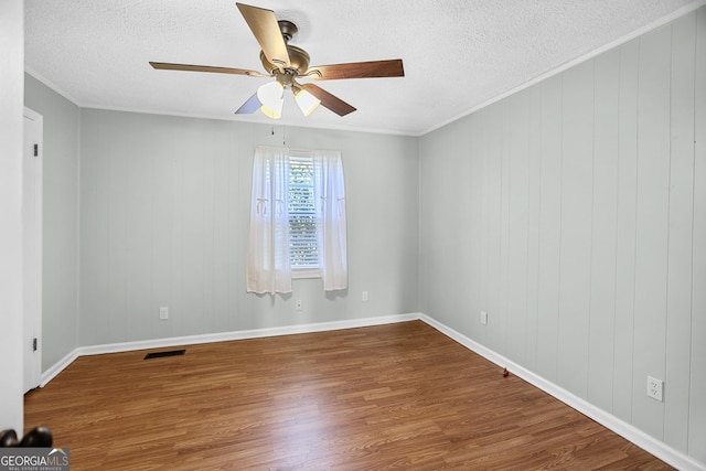 empty room featuring a textured ceiling, visible vents, wood finished floors, and ornamental molding