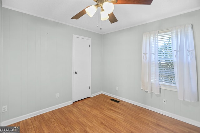 empty room featuring visible vents, ornamental molding, ceiling fan, wood finished floors, and baseboards