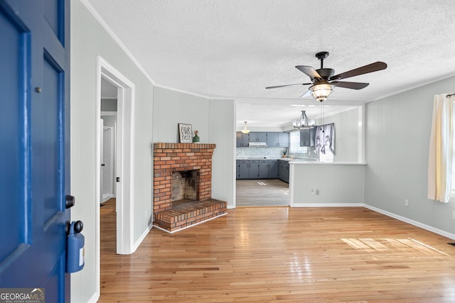 unfurnished living room featuring ceiling fan with notable chandelier, light wood finished floors, a brick fireplace, and crown molding