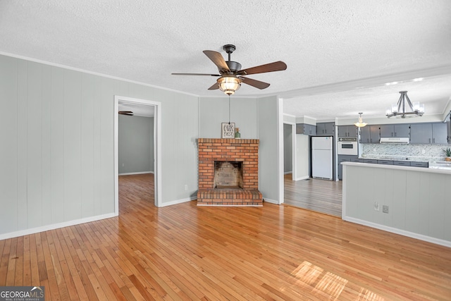 unfurnished living room with light wood-type flooring, a brick fireplace, crown molding, and ceiling fan with notable chandelier