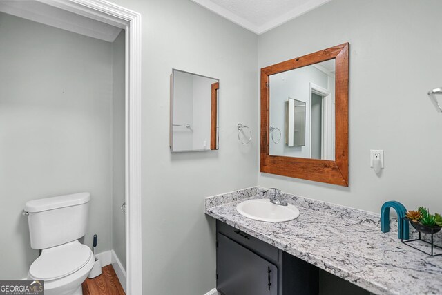 half bathroom featuring wood finished floors, vanity, toilet, and baseboards