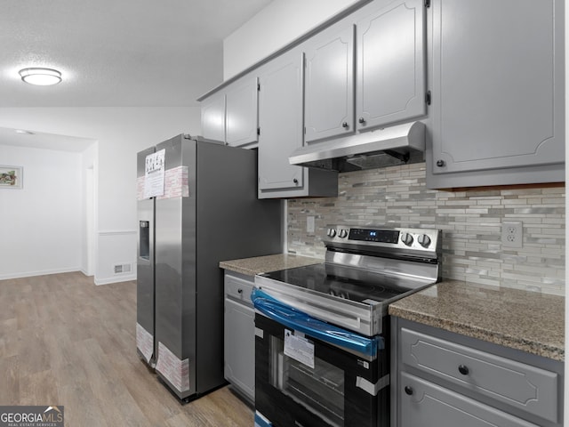 kitchen with gray cabinetry, under cabinet range hood, appliances with stainless steel finishes, light wood-type flooring, and dark countertops