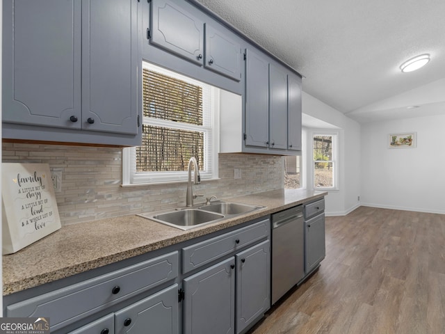 kitchen with a sink, lofted ceiling, stainless steel dishwasher, and gray cabinetry