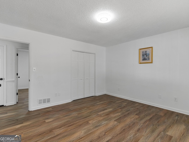 unfurnished bedroom with baseboards, visible vents, dark wood-style flooring, a textured ceiling, and a closet