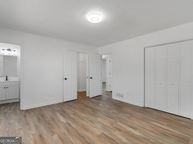 unfurnished bedroom featuring light wood-style floors, ensuite bath, visible vents, and a sink