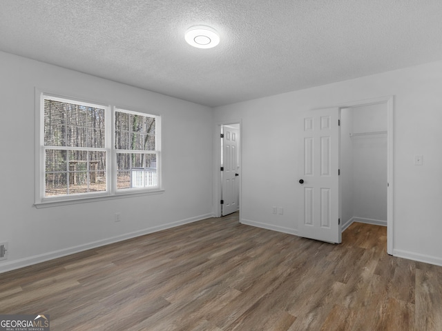 unfurnished bedroom featuring a textured ceiling, baseboards, and wood finished floors