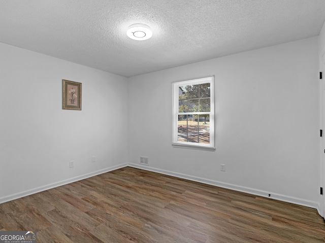 empty room featuring dark wood-style floors, visible vents, baseboards, and a textured ceiling