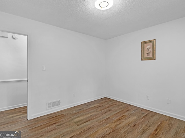 empty room featuring baseboards, a textured ceiling, visible vents, and wood finished floors