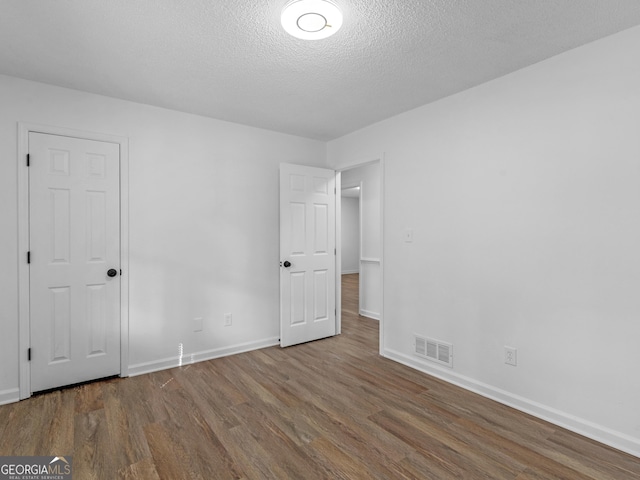 unfurnished bedroom featuring baseboards, a textured ceiling, visible vents, and wood finished floors