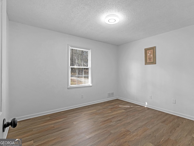 empty room with a textured ceiling, dark wood-style flooring, visible vents, and baseboards