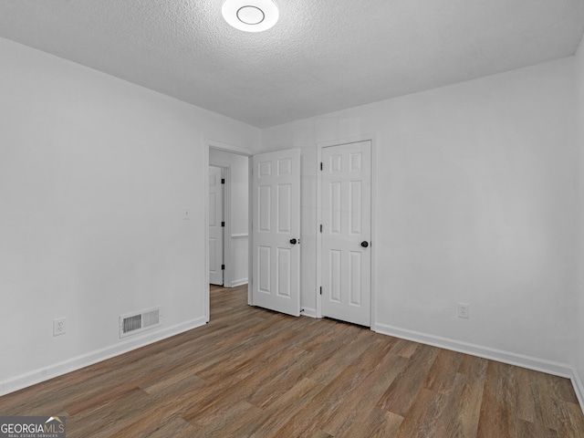 unfurnished bedroom with visible vents, a textured ceiling, baseboards, and wood finished floors