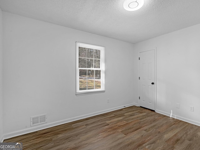 empty room featuring visible vents, dark wood finished floors, a textured ceiling, and baseboards