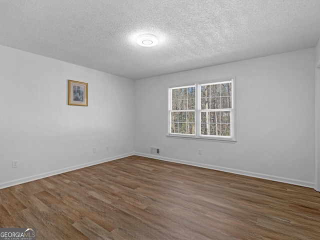 unfurnished room with dark wood-style floors, visible vents, and baseboards