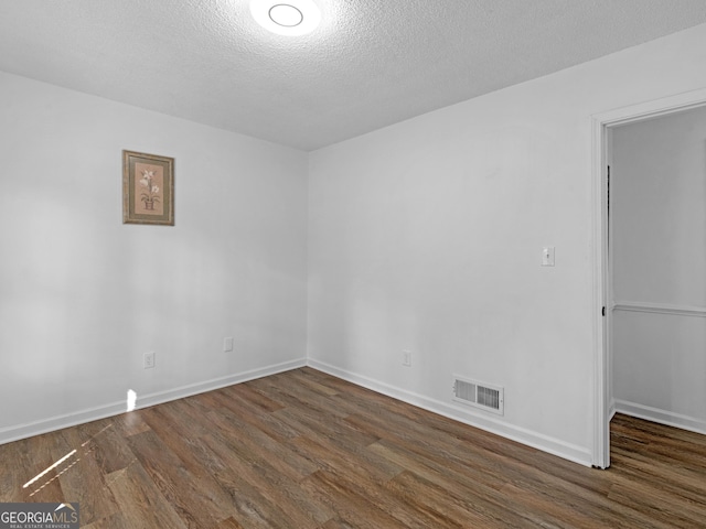 empty room with dark wood-style flooring, visible vents, a textured ceiling, and baseboards