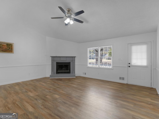 unfurnished living room with a fireplace with raised hearth, lofted ceiling, wood finished floors, a ceiling fan, and baseboards