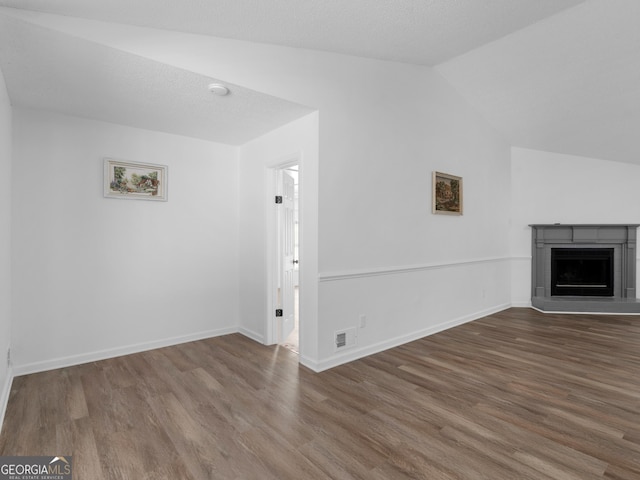 unfurnished living room featuring dark wood-style floors, lofted ceiling, a fireplace with raised hearth, and visible vents