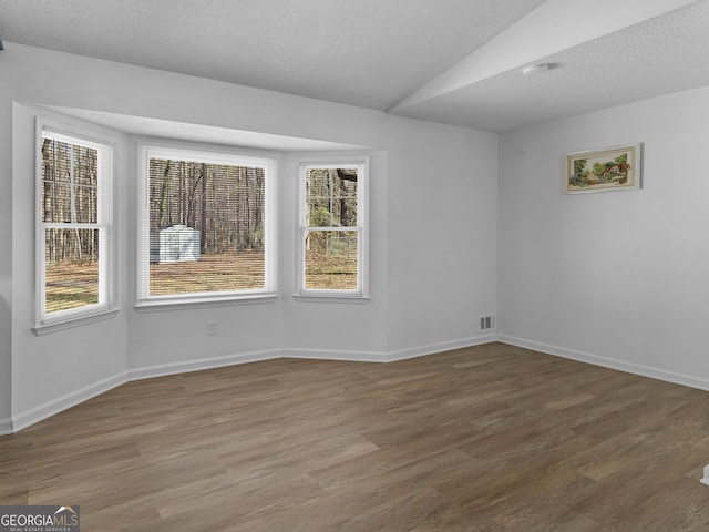 empty room featuring a textured ceiling, dark wood-type flooring, and baseboards