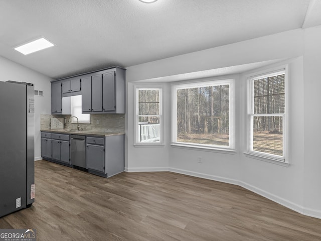 kitchen with lofted ceiling, gray cabinetry, stainless steel appliances, a sink, and dark wood finished floors